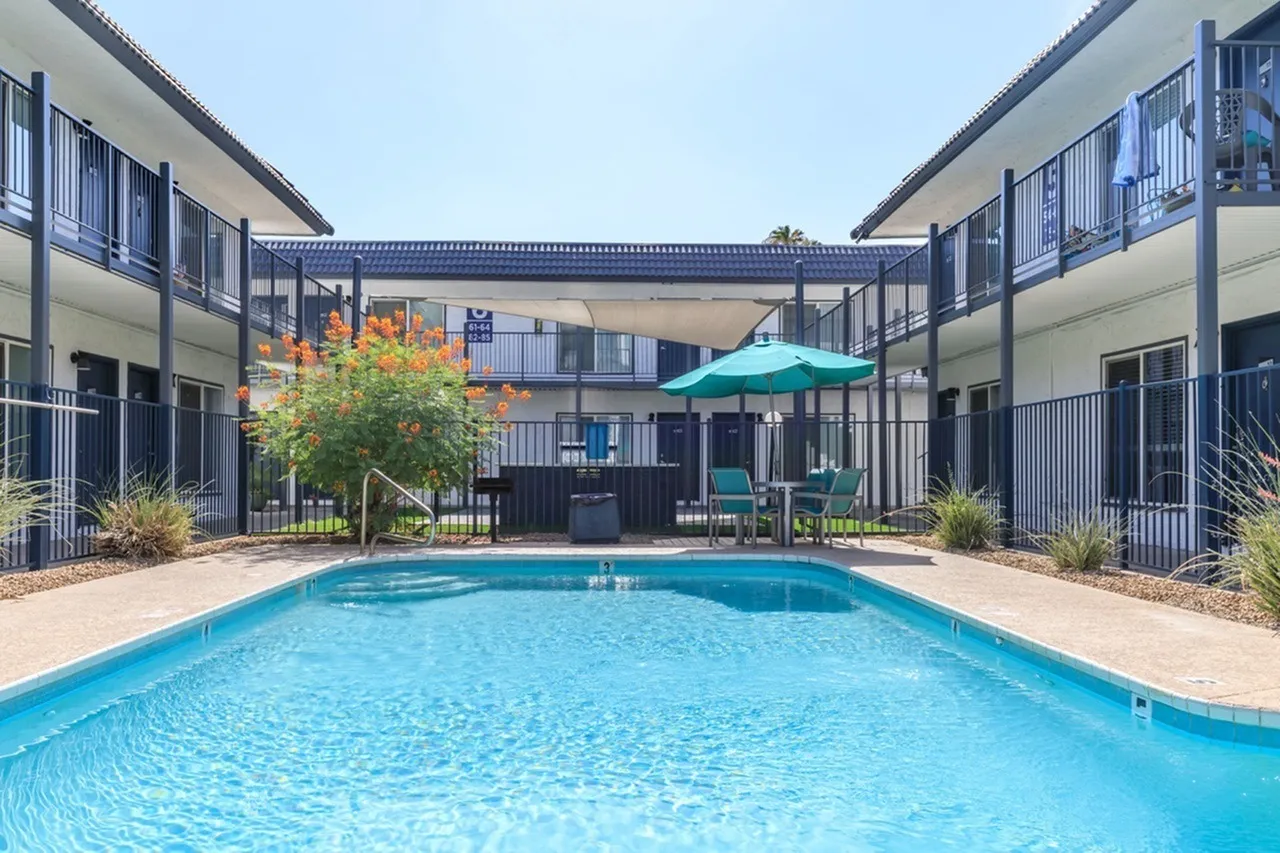 Courtyard pool area, bright blue water, turquoise umbrella, landscaping, multi-story residential building