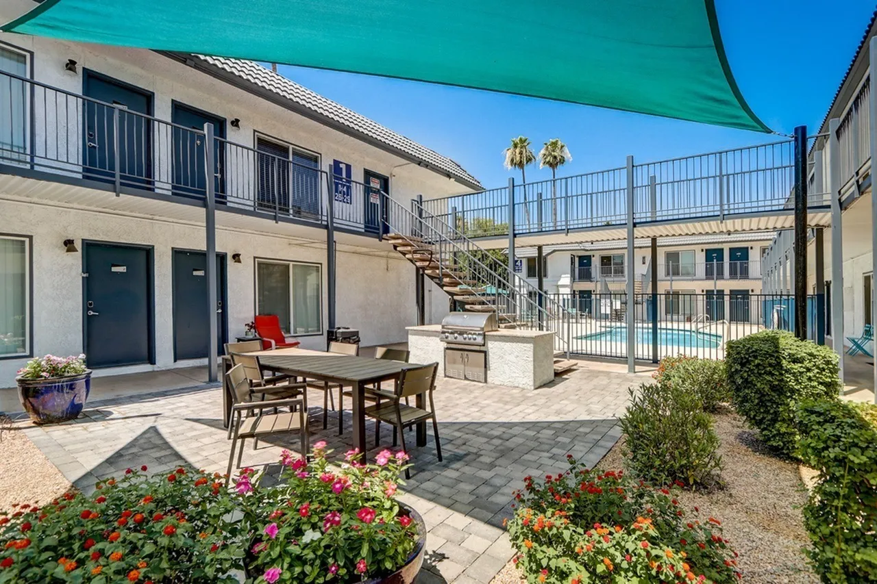 Courtyard with dining table, turquoise shade canopy, flowering planters, stucco buildings