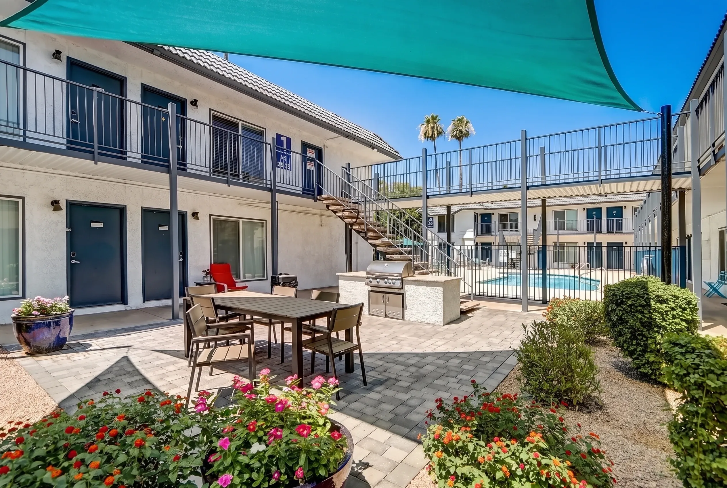 Courtyard with dining table, turquoise shade canopy, flowering planters, stucco buildings