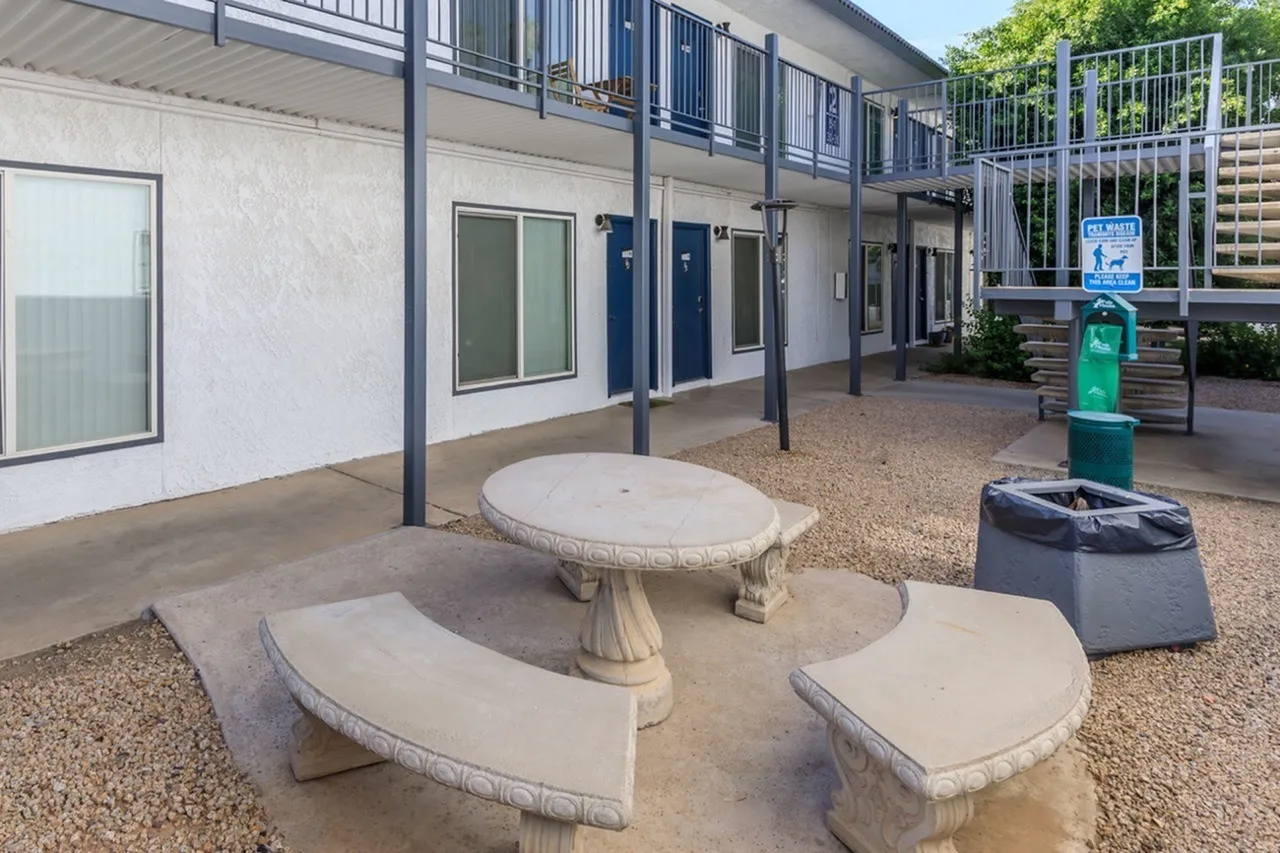 Courtyard with concrete round and curved bench seating, gravel ground, white building, metal railings