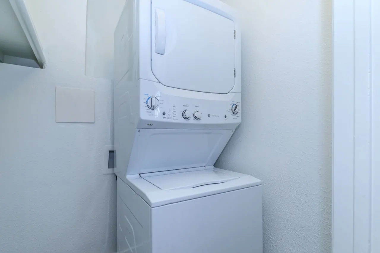 Laundry closet, white stacked washer dryer unit, white walls, light fixture