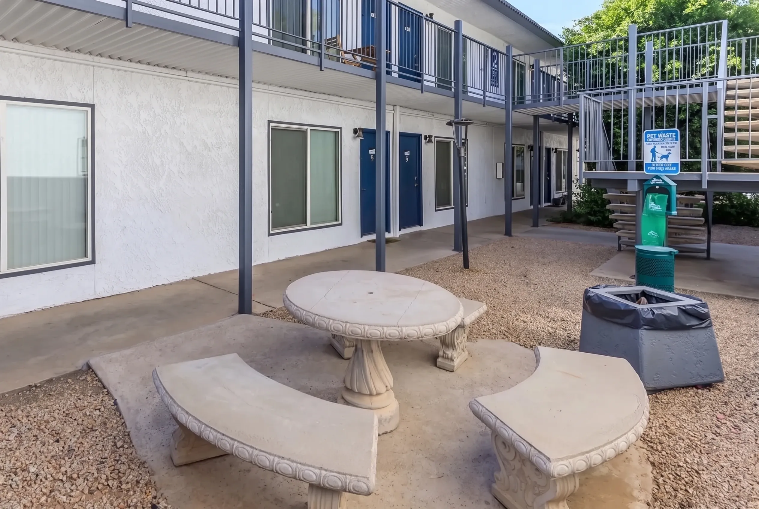 Courtyard with concrete round and curved bench seating, gravel ground, white building, metal railings