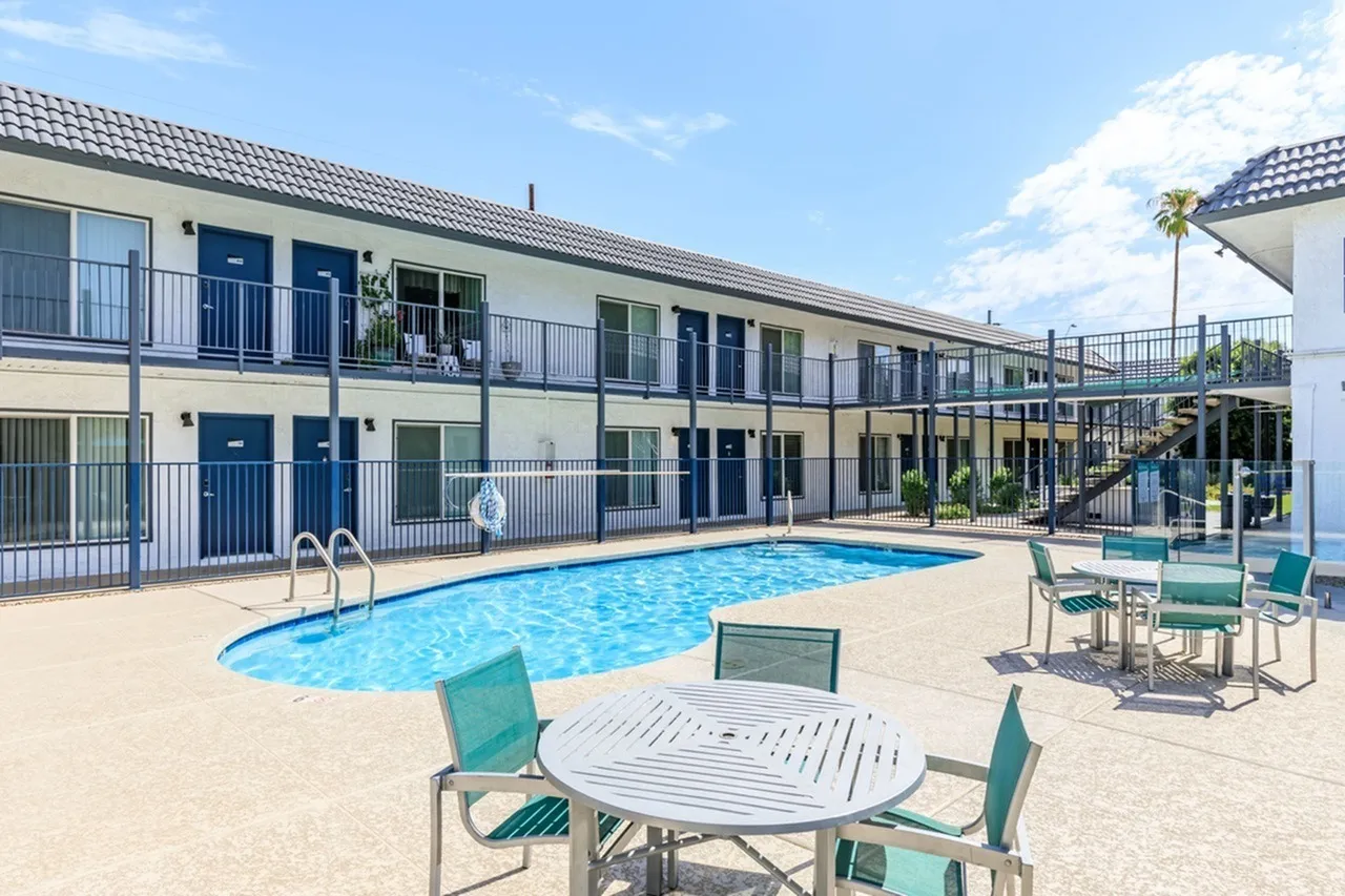Pool area with turquoise lounge chairs, dining tables, two-story residential building, metal railings