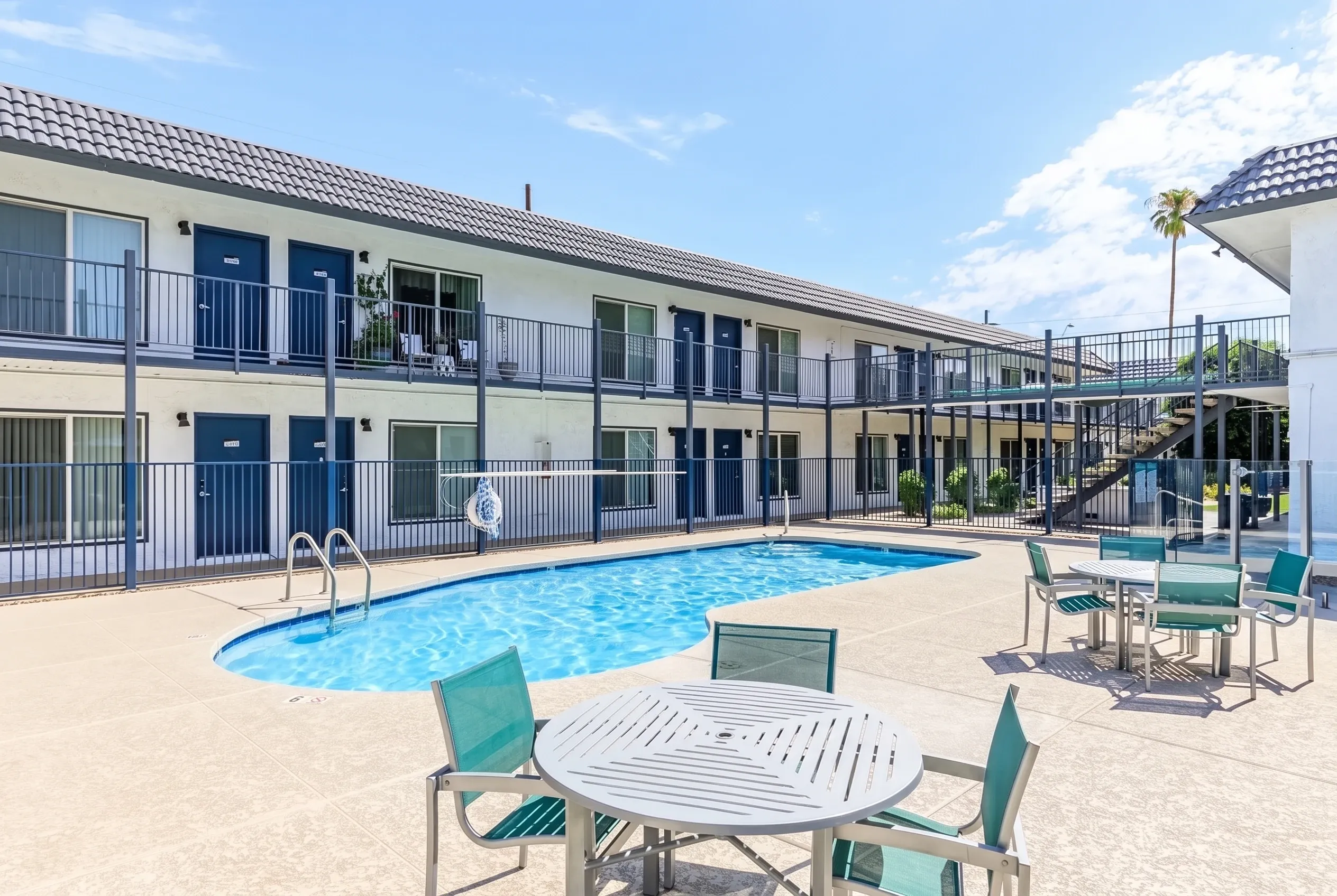 Pool area with turquoise lounge chairs, dining tables, two-story residential building, metal railings
