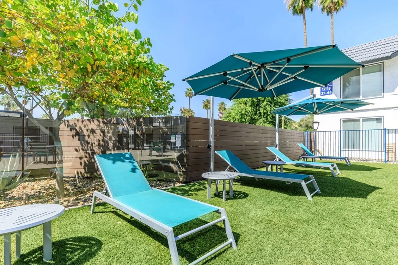 Outdoor courtyard, blue lounge chairs, cantilever umbrellas, turf lawn, mature trees