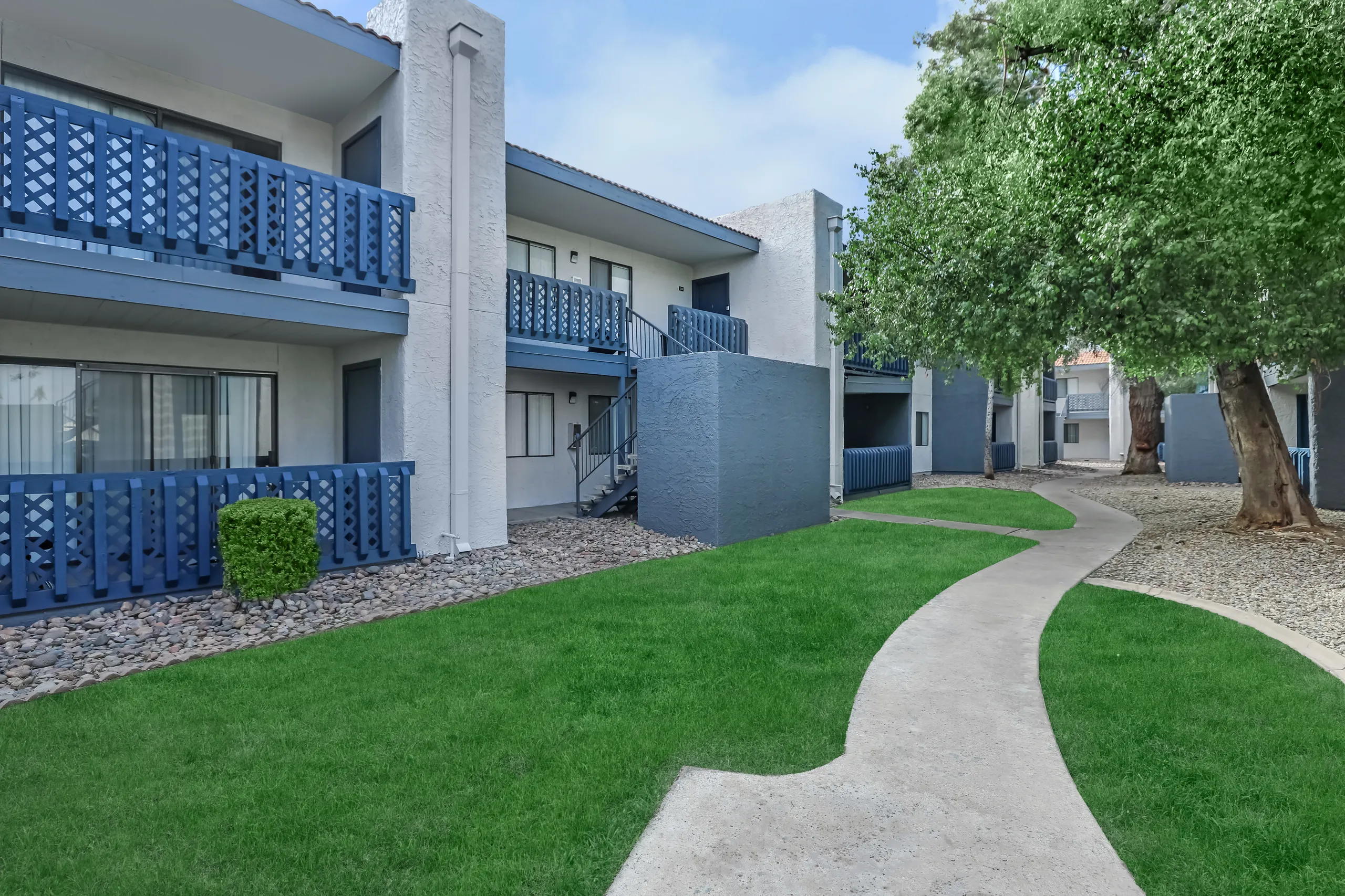 Landscaped courtyard walkway between apartment buildings with blue balcony railings