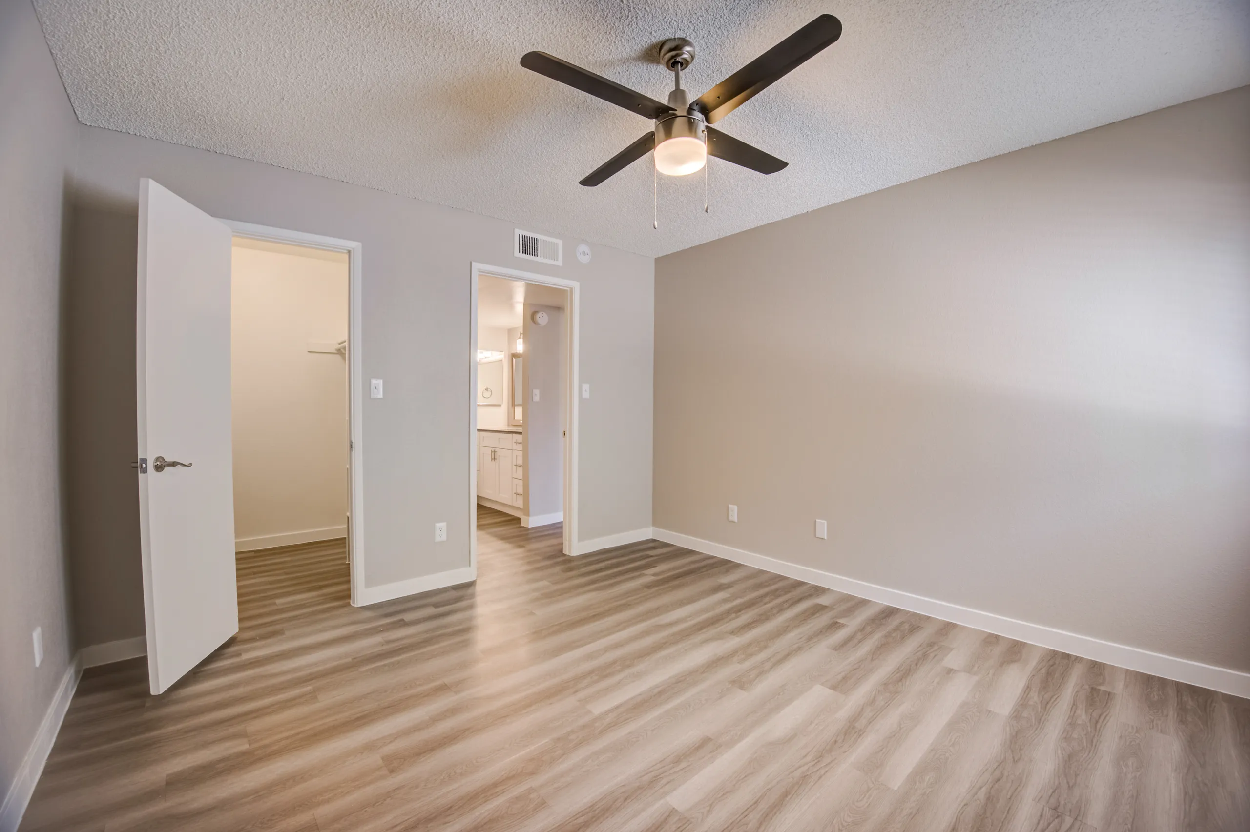 Primary bedroom with ceiling fan and view into walk-in closet and ensuite bathroom