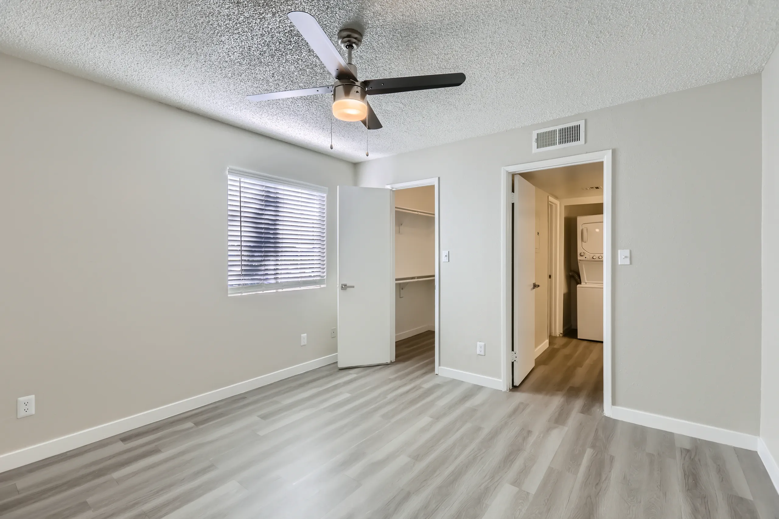 Primary bedroom with ceiling fan and view into walk-in closet and in-unit laundry area