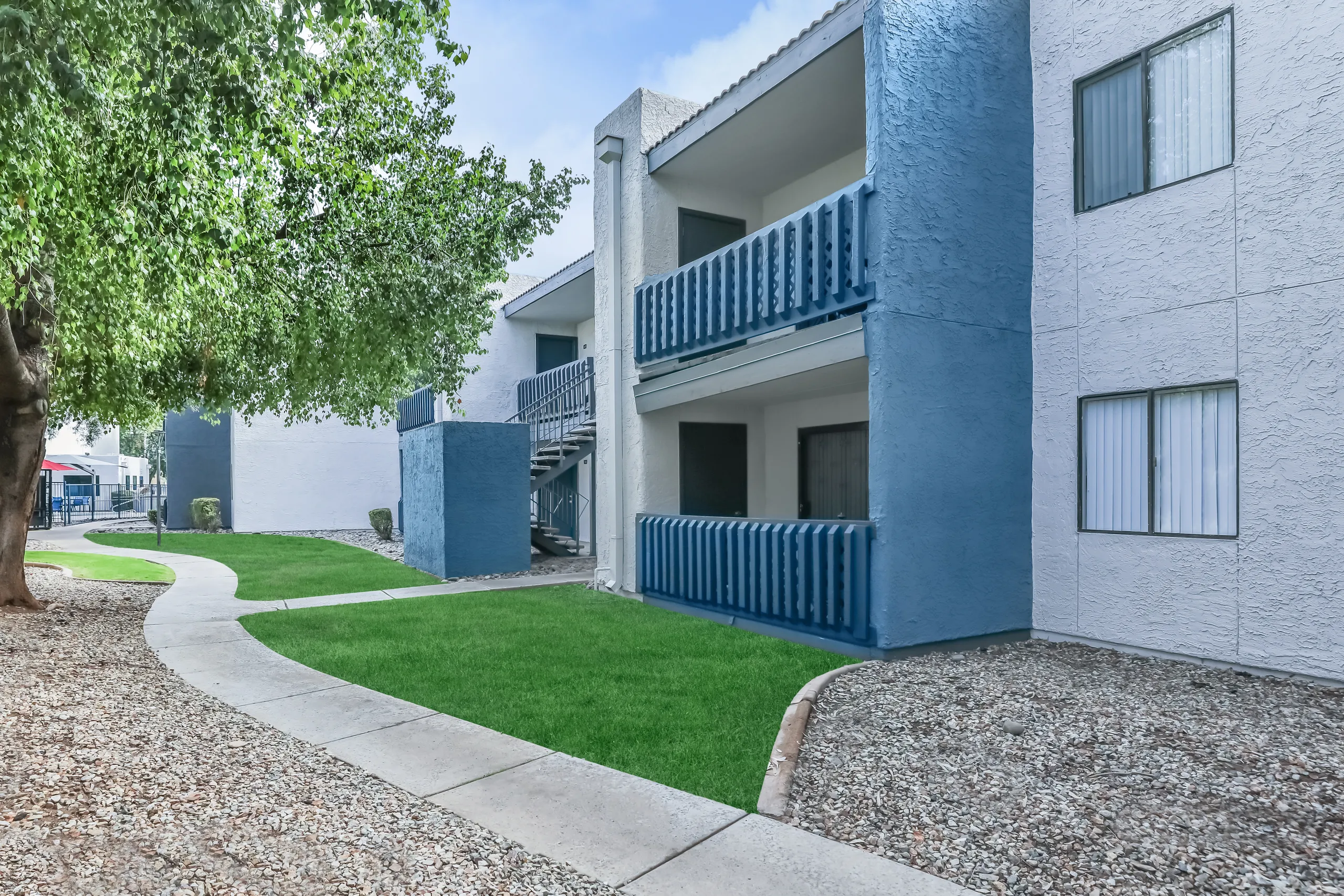 Ground-floor apartment entrances with blue balcony accents and mature trees