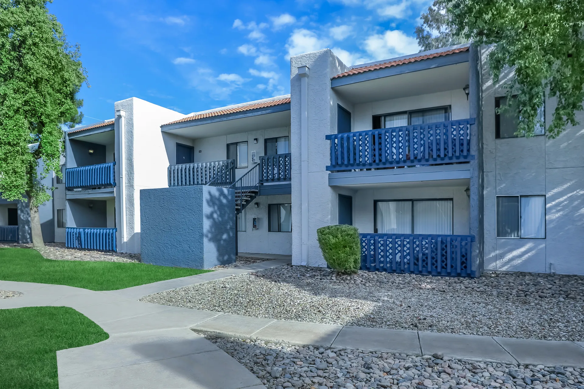 Two-story apartment building exterior with blue balconies and desert rock landscaping