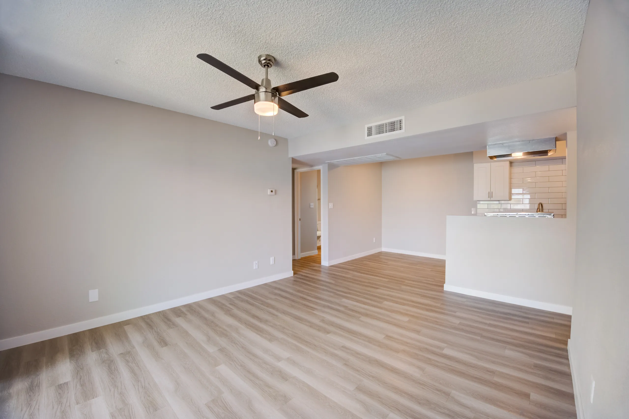 Living room with ceiling fan and view into kitchen