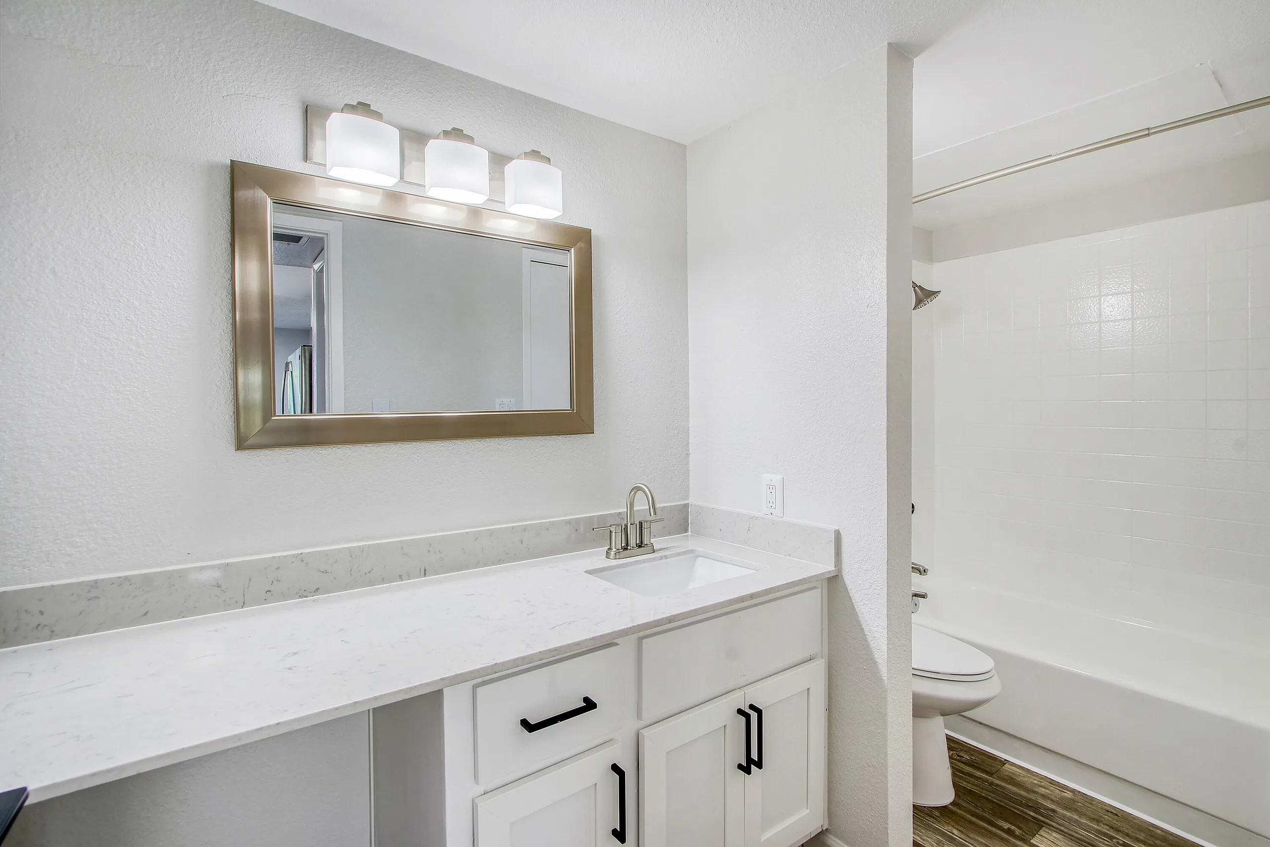 Primary bathroom, white shaker cabinetry, quartz countertops, framed mirror with lighting