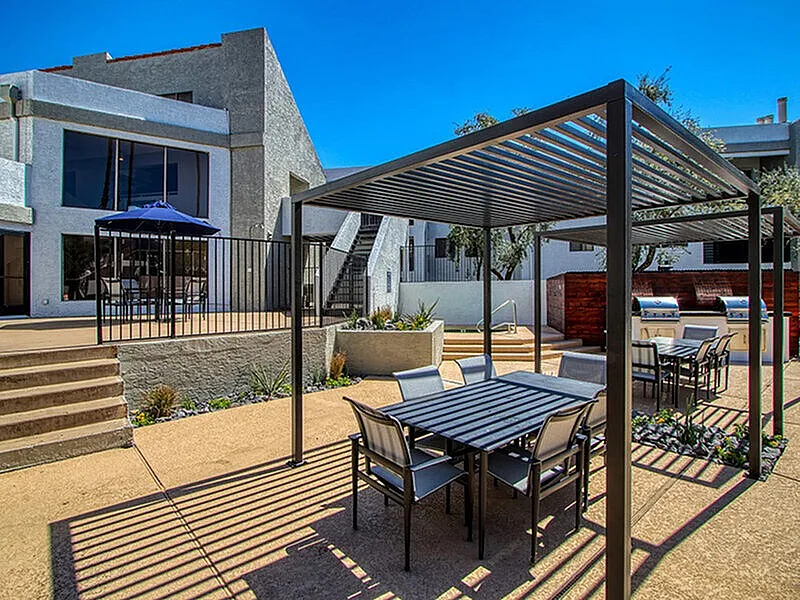 Patio area, black metal pergola, striped dining table, wood-style plank flooring, clear blue sky