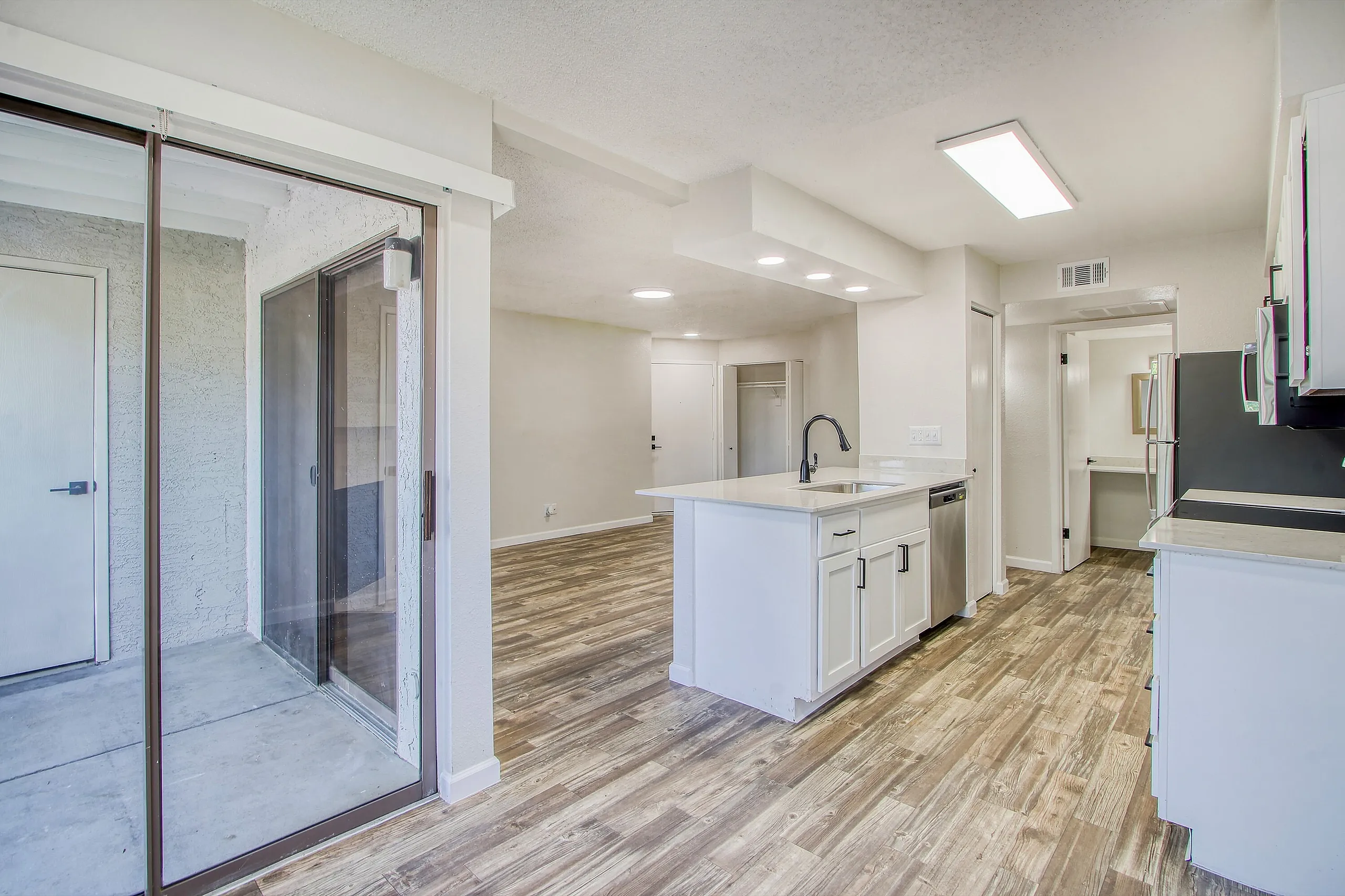 Kitchen with white cabinetry, quartz countertops, stainless appliances, wood-style plank flooring, primary bathroom with shower enclosure visible
