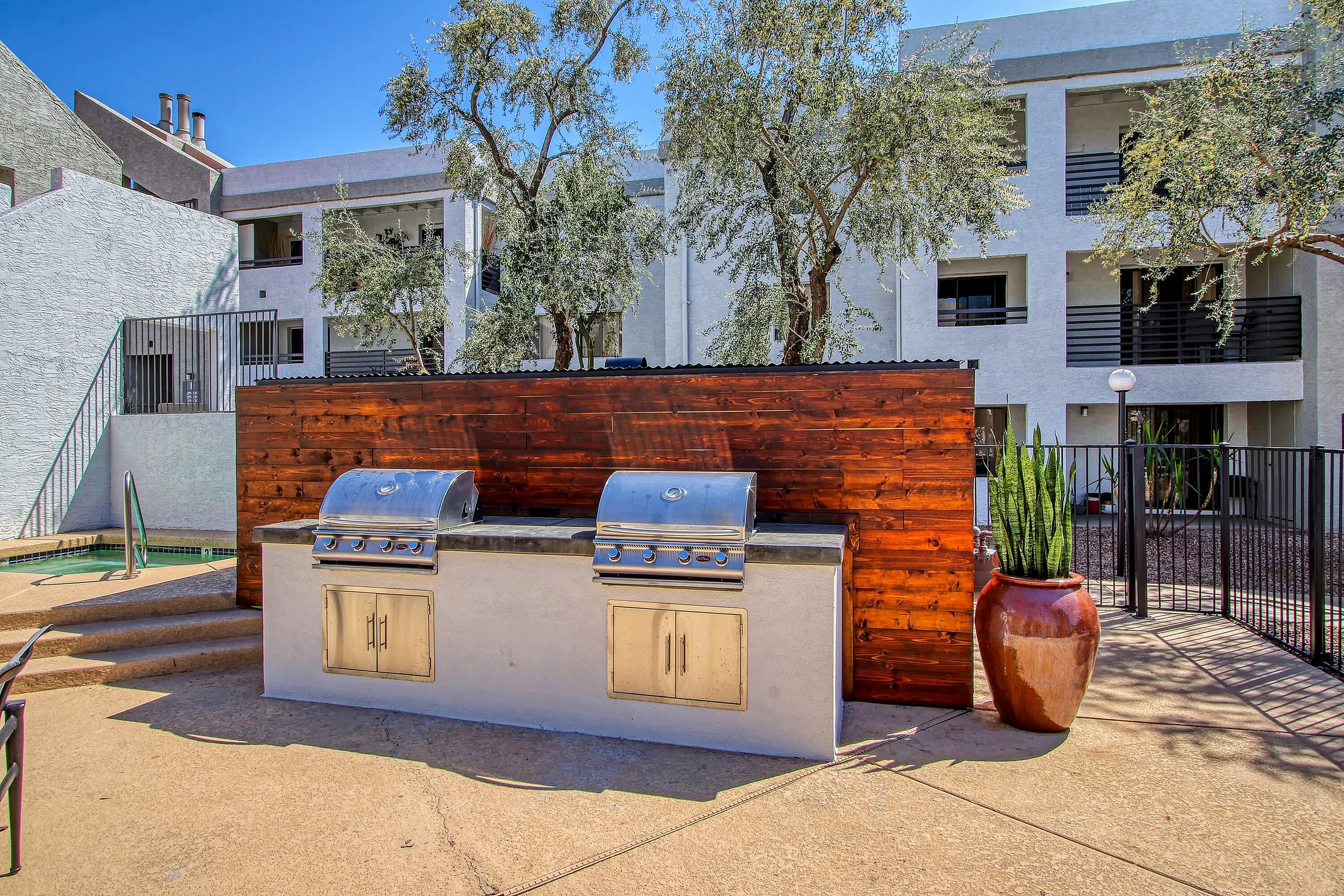 Outdoor courtyard with dual built-in blue grills, stucco base with wood cabinet doors, wooden privacy screen backdrop