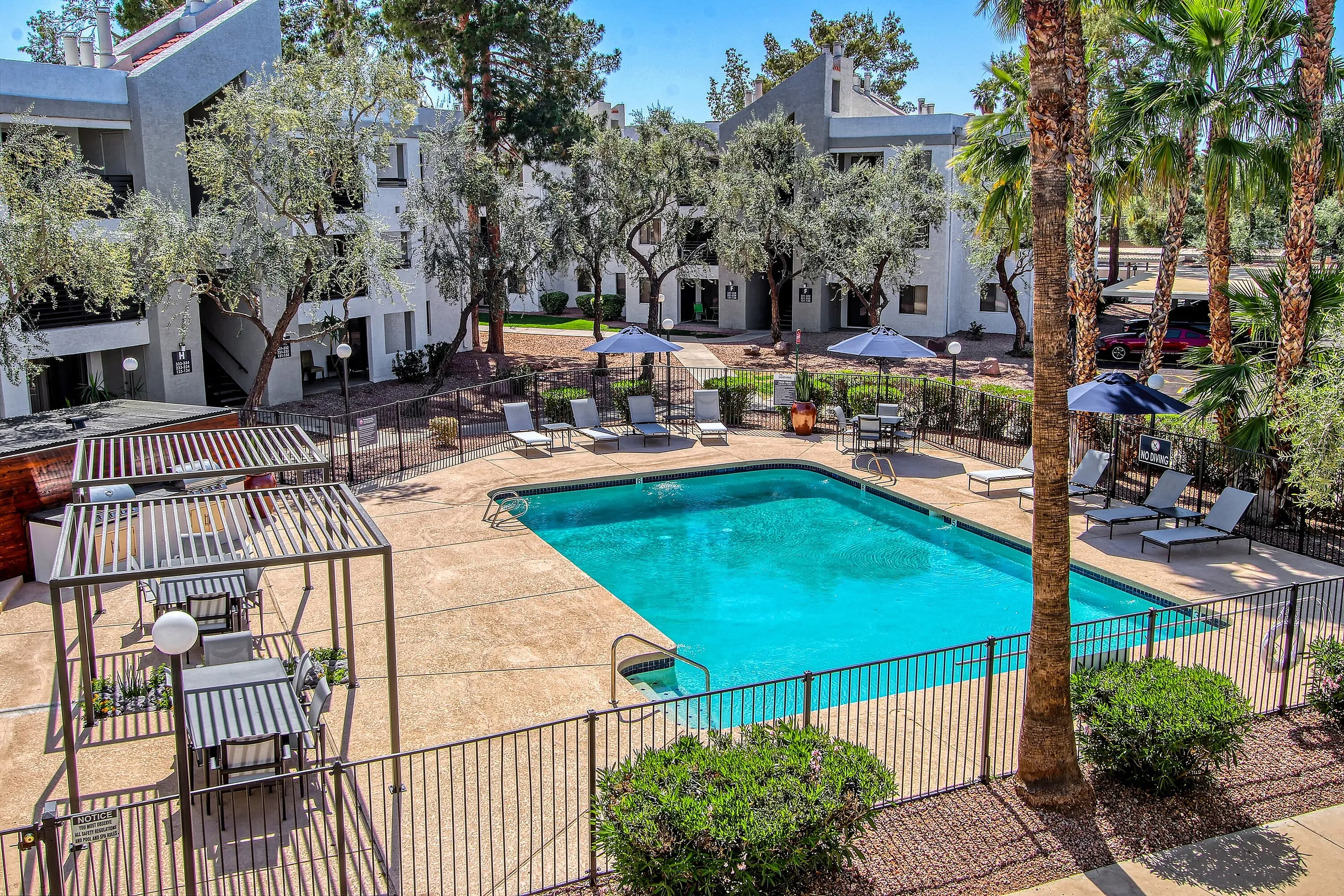 Resort-style pool, lounge chairs, palm trees, surrounding courtyard with modern white buildings