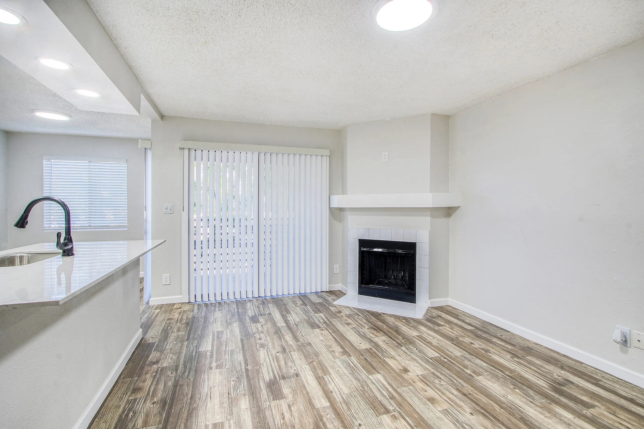 Living room with fireplace, kitchen with white cabinetry and quartz countertops, wood-style plank flooring, glass patio doors