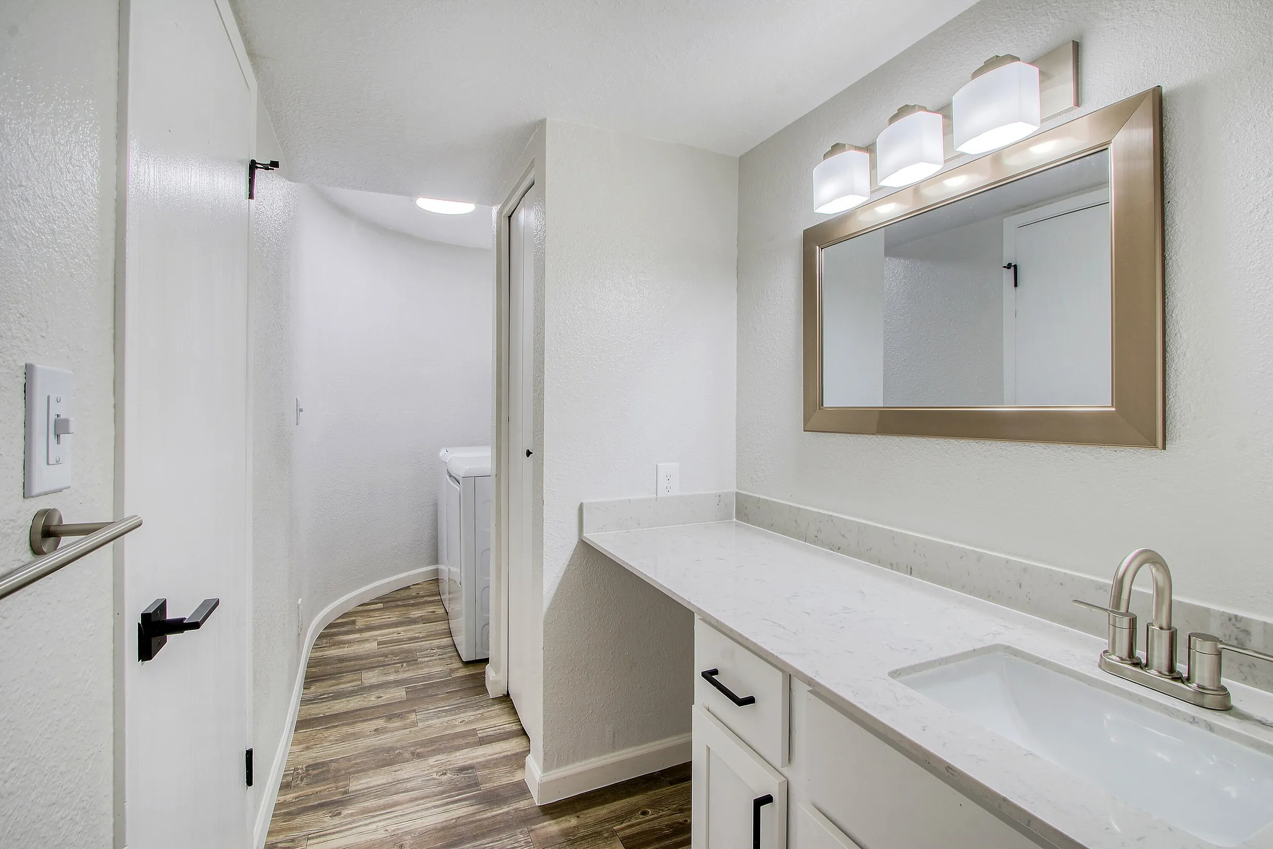 Bathroom, dual vanity with white cabinetry, quartz countertop, wood-style plank flooring, framed mirror with light fixture
