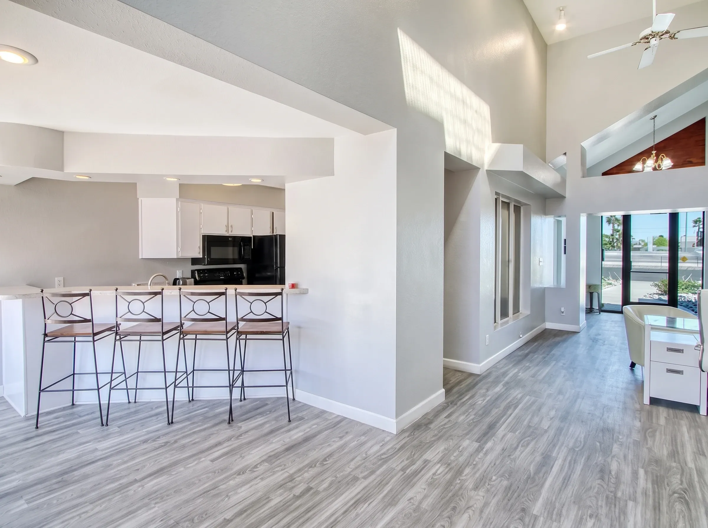 Open kitchen and living room, wood-style plank flooring, white cabinetry, black appliances, island seating