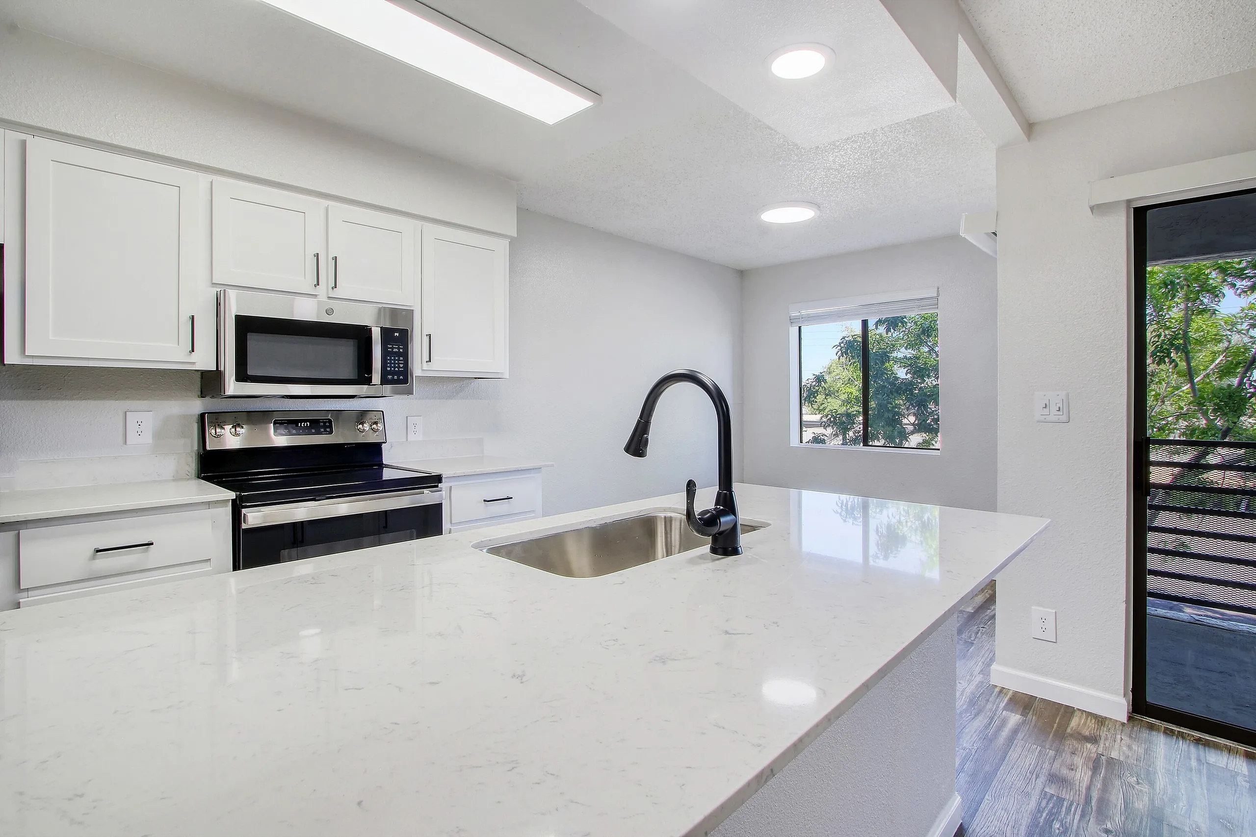 Kitchen, white shaker cabinetry, quartz countertops, black stainless appliances, black faucet, wood-style plank flooring