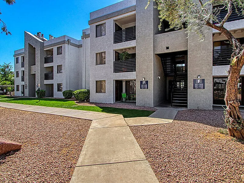 Multi-story residential building, concrete facade, horizontal railings, ground level courtyard with gravel and concrete pathway