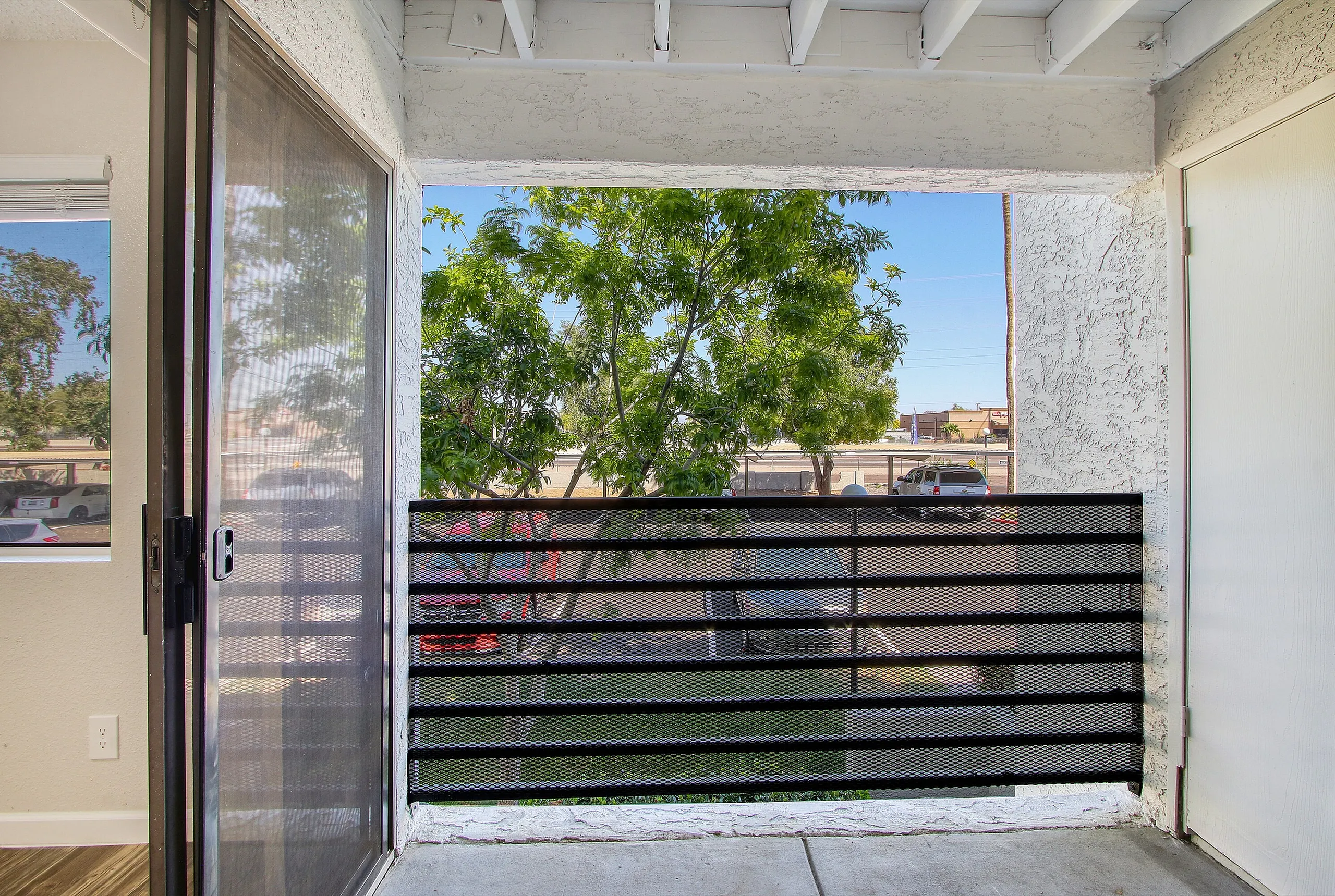 Balcony, black metal railing, concrete flooring, sliding glass door, tree and city views
