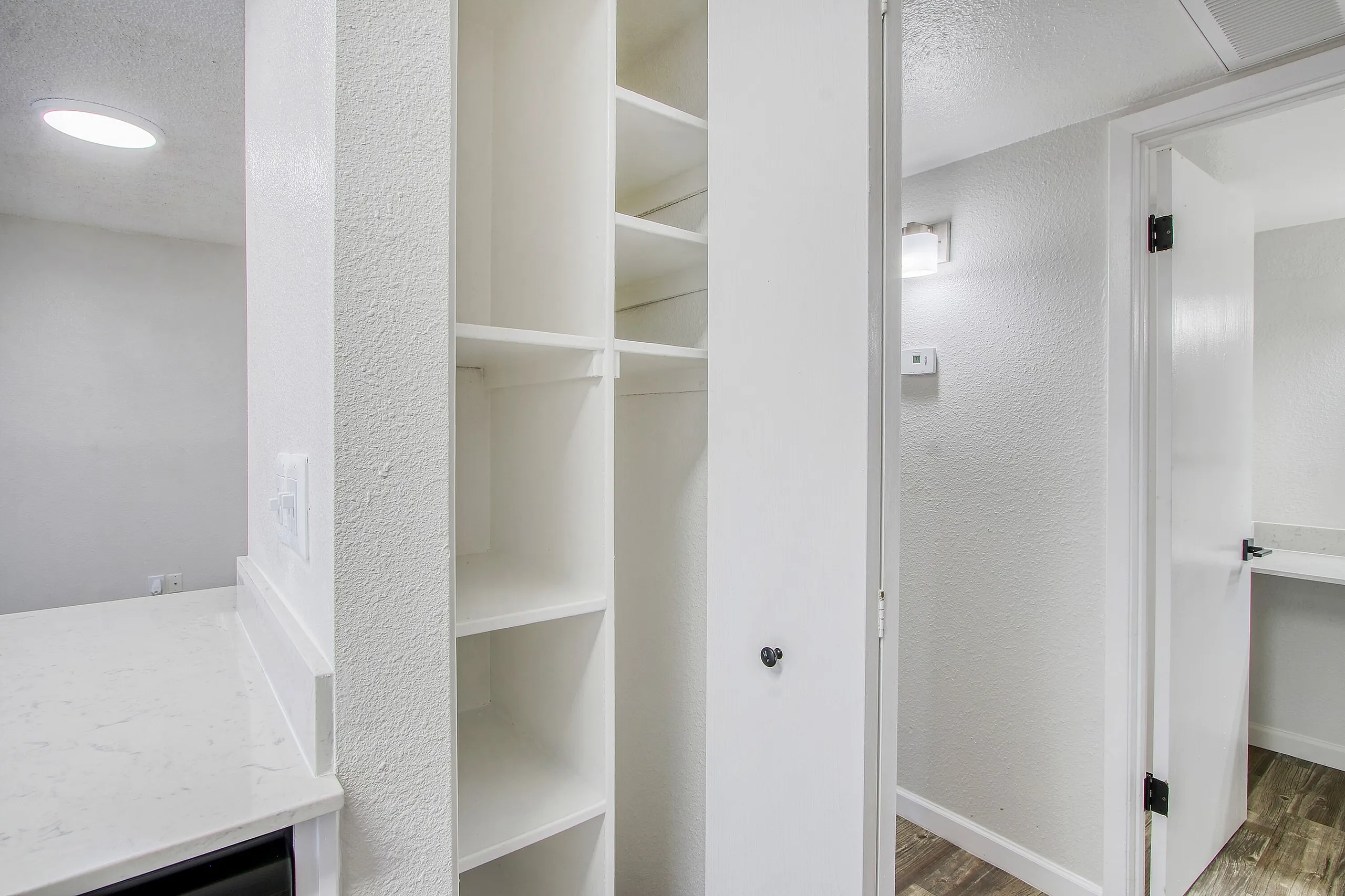 Walk-in closet, white built-in shelving, textured wall panel, wood-style plank flooring