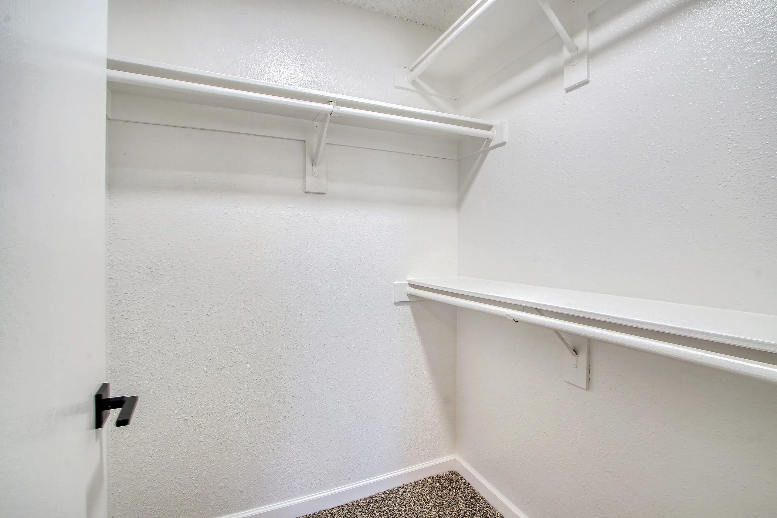 Walk-in closet, white walls, shelving and rod, carpet flooring