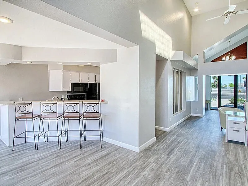 Open kitchen and living room, wood-style plank flooring, white cabinetry, black appliances, island seating