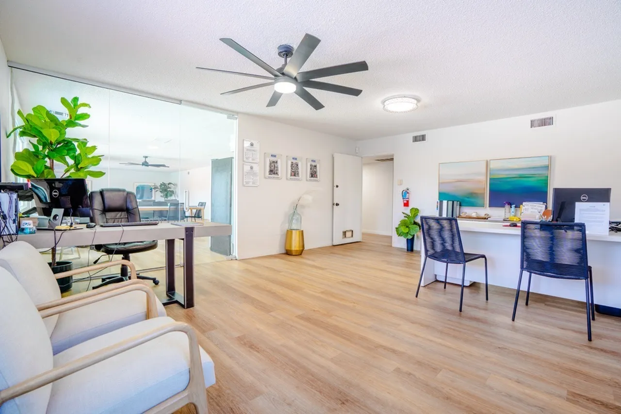 Open office area, wood-style plank flooring, modern ceiling fan, workspace with desk and chairs