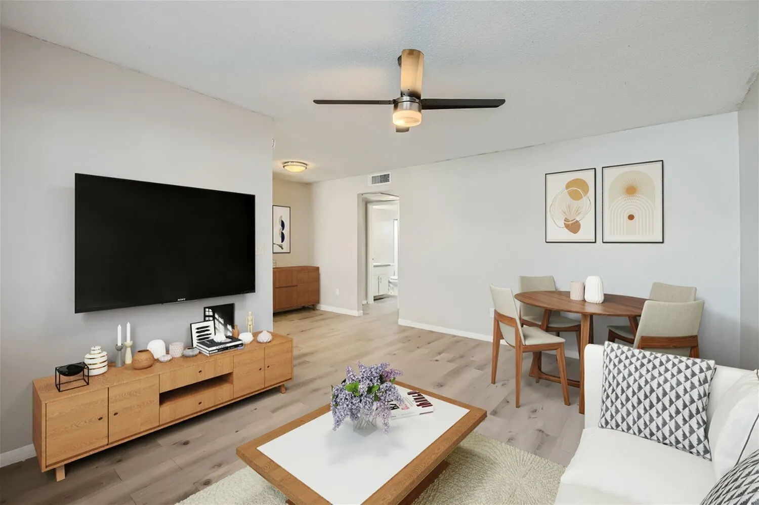 Living room with wood-style plank flooring, ceiling fan, flat-screen TV mounted on wall, wood media console