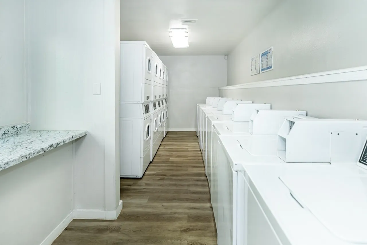 Laundry room, stacked white washers and dryers, marble countertop, wood-style plank flooring