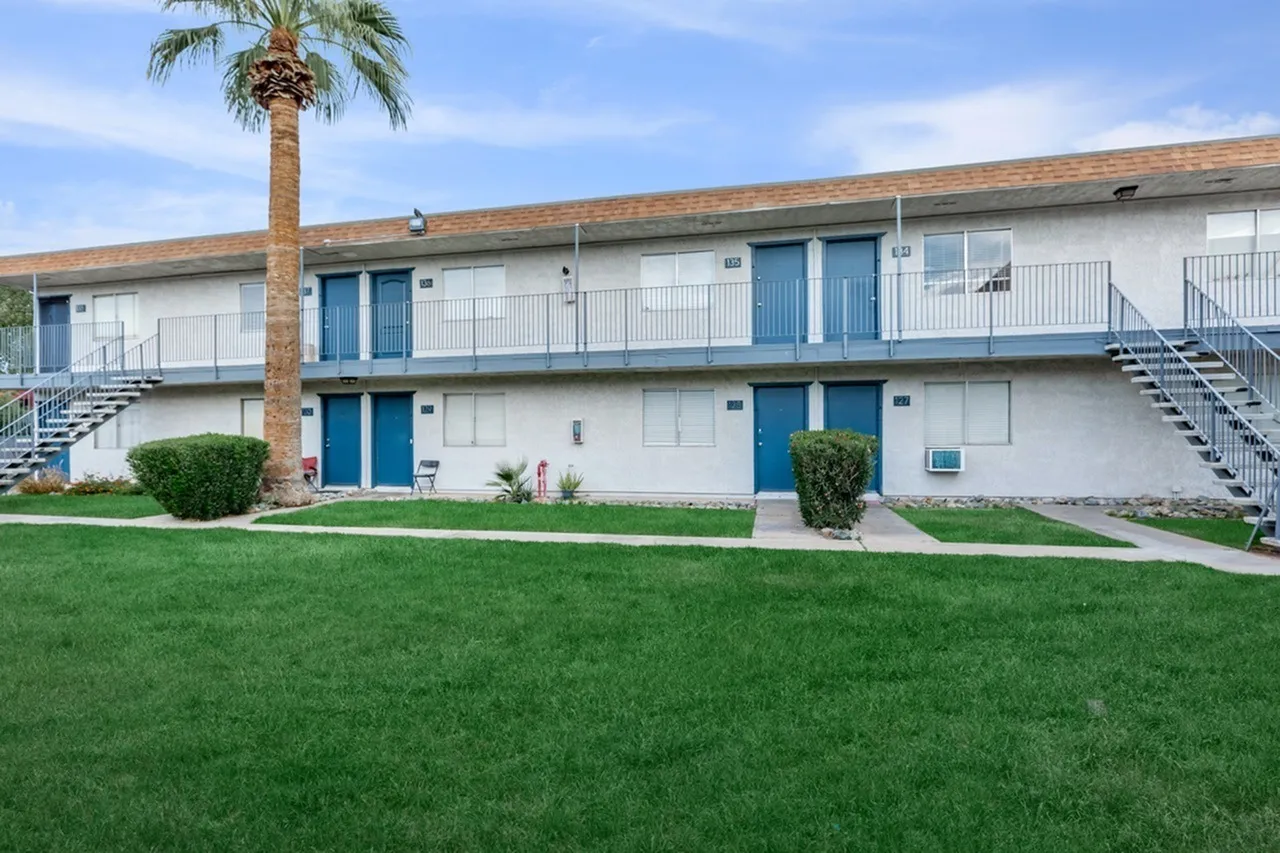 Two-story residential building, blue entry doors, white walls, palm tree, manicured lawn, metal railings