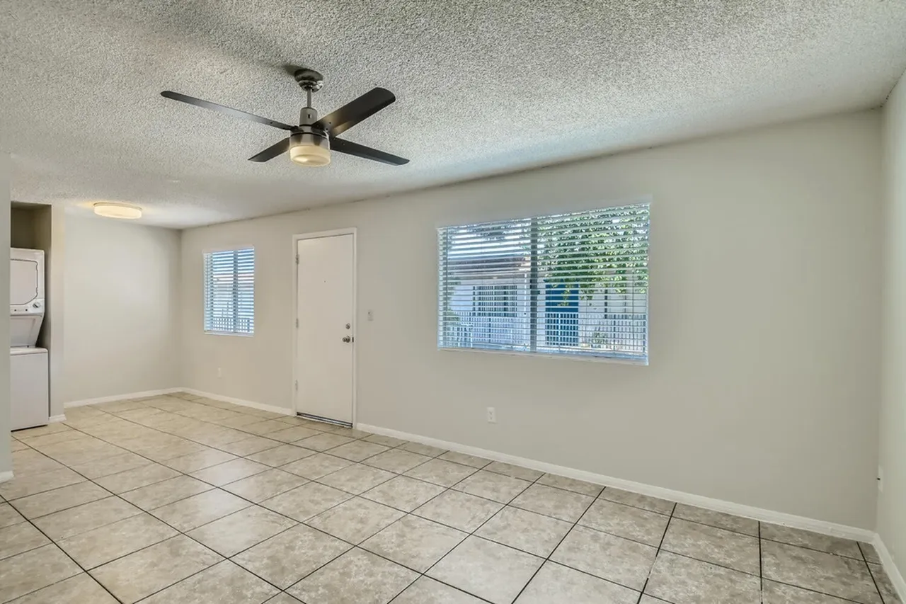 Living room with tile flooring, ceiling fan, windows with blinds, entry door