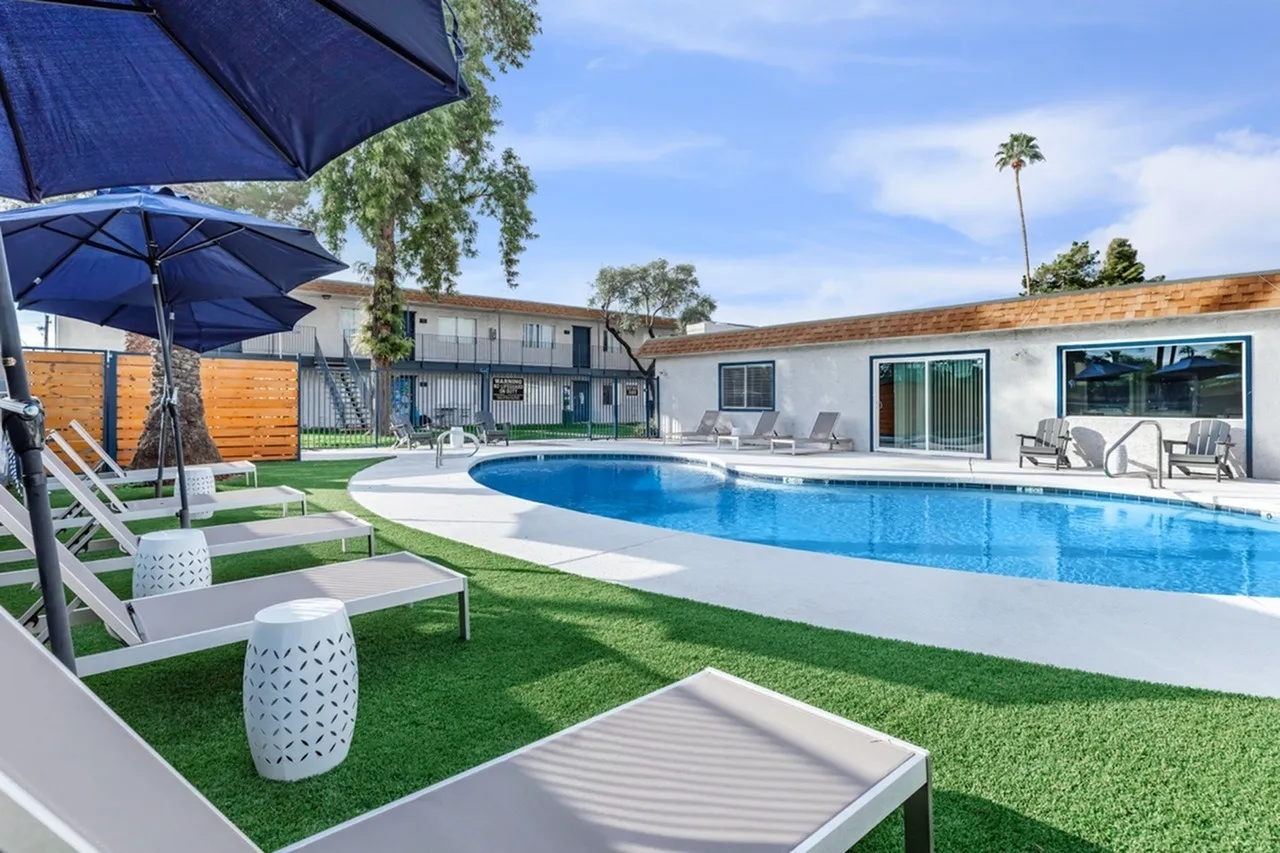 Pool area, blue swimming pool, lounge chairs, blue umbrellas, artificial turf, wooden privacy fence