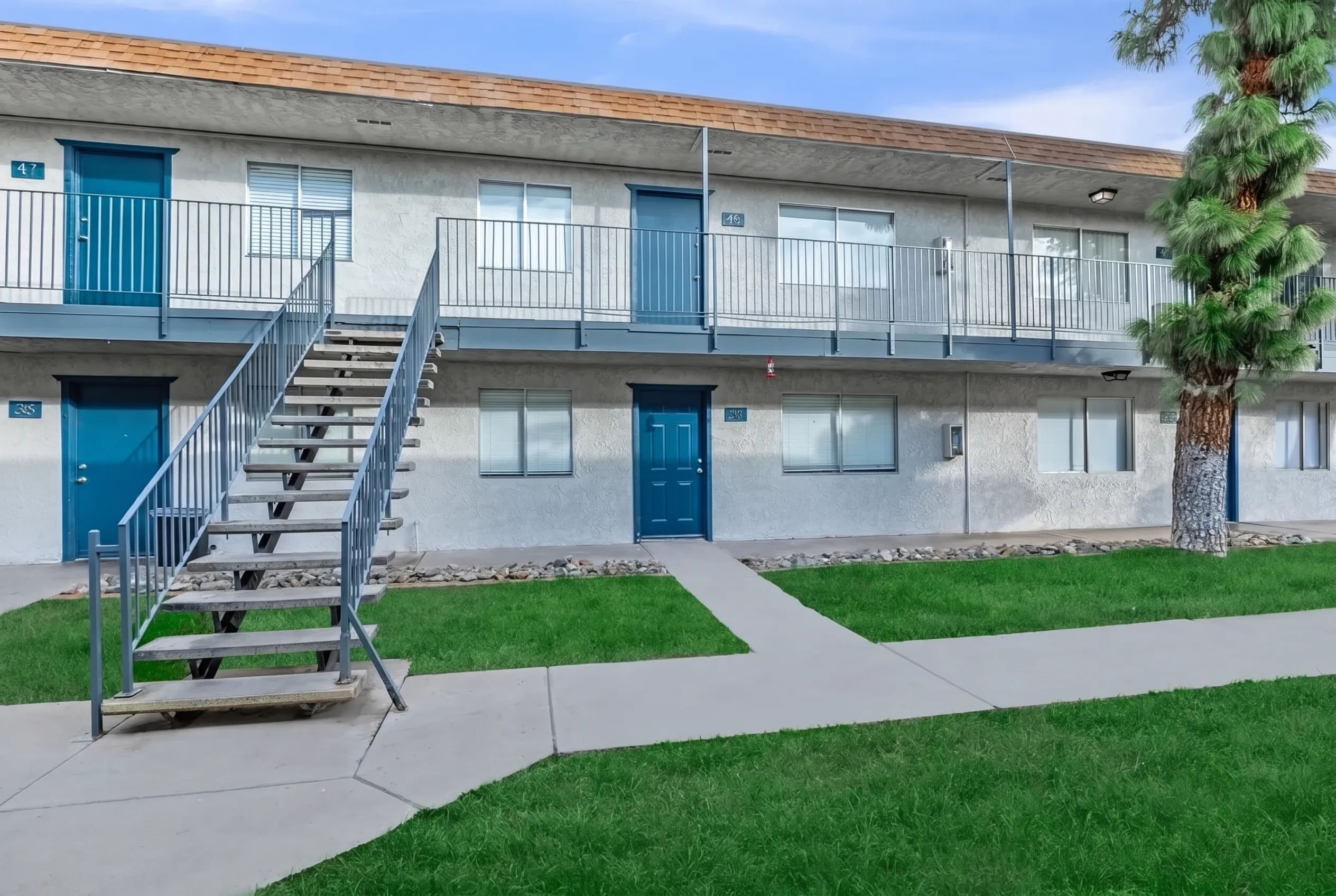 Two-story apartment building, blue entry doors, metal railings, concrete walkway, manicured lawn