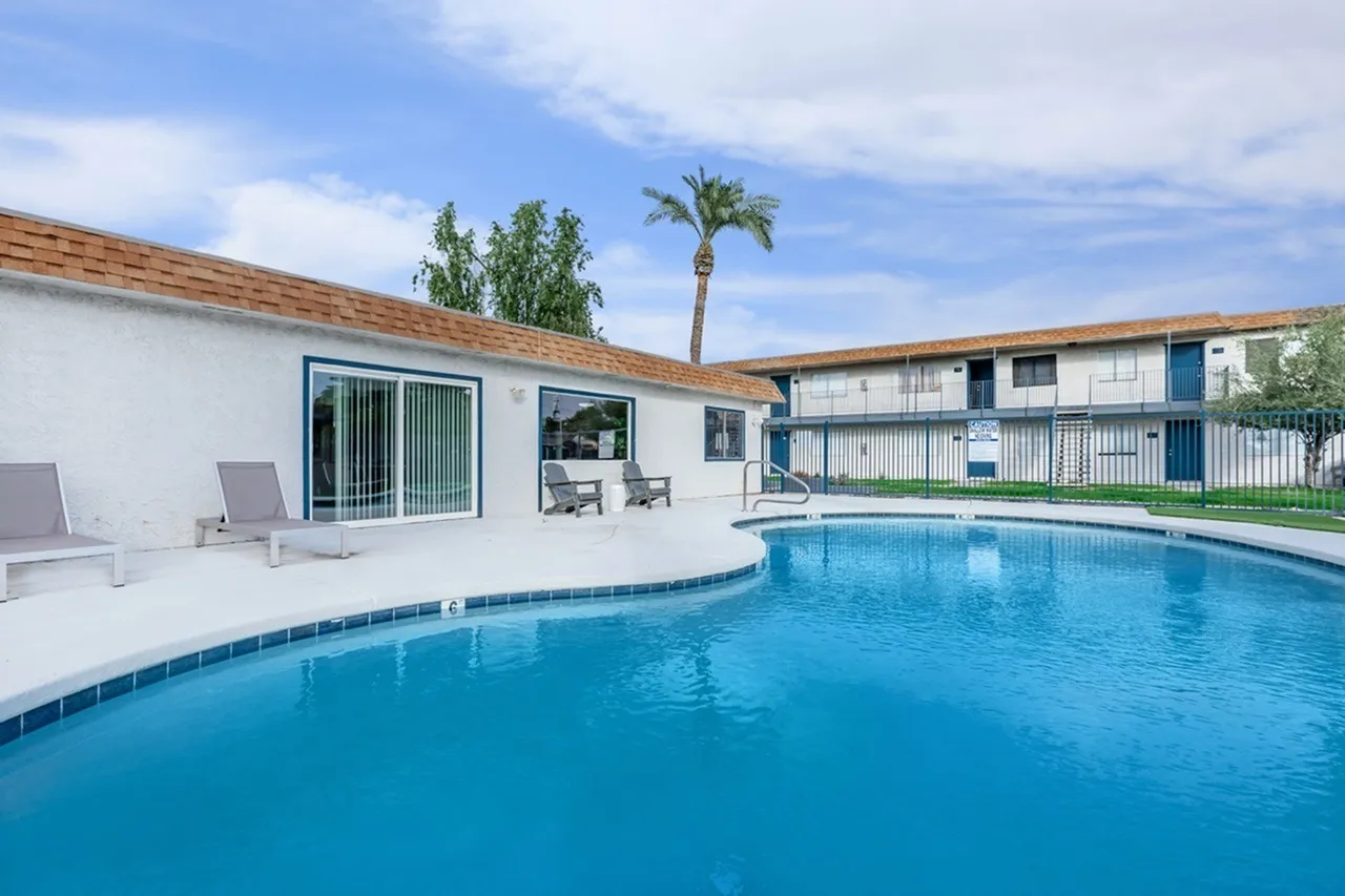 Swimming pool with blue water, white deck, lounge chairs, white building with glass doors, palm tree