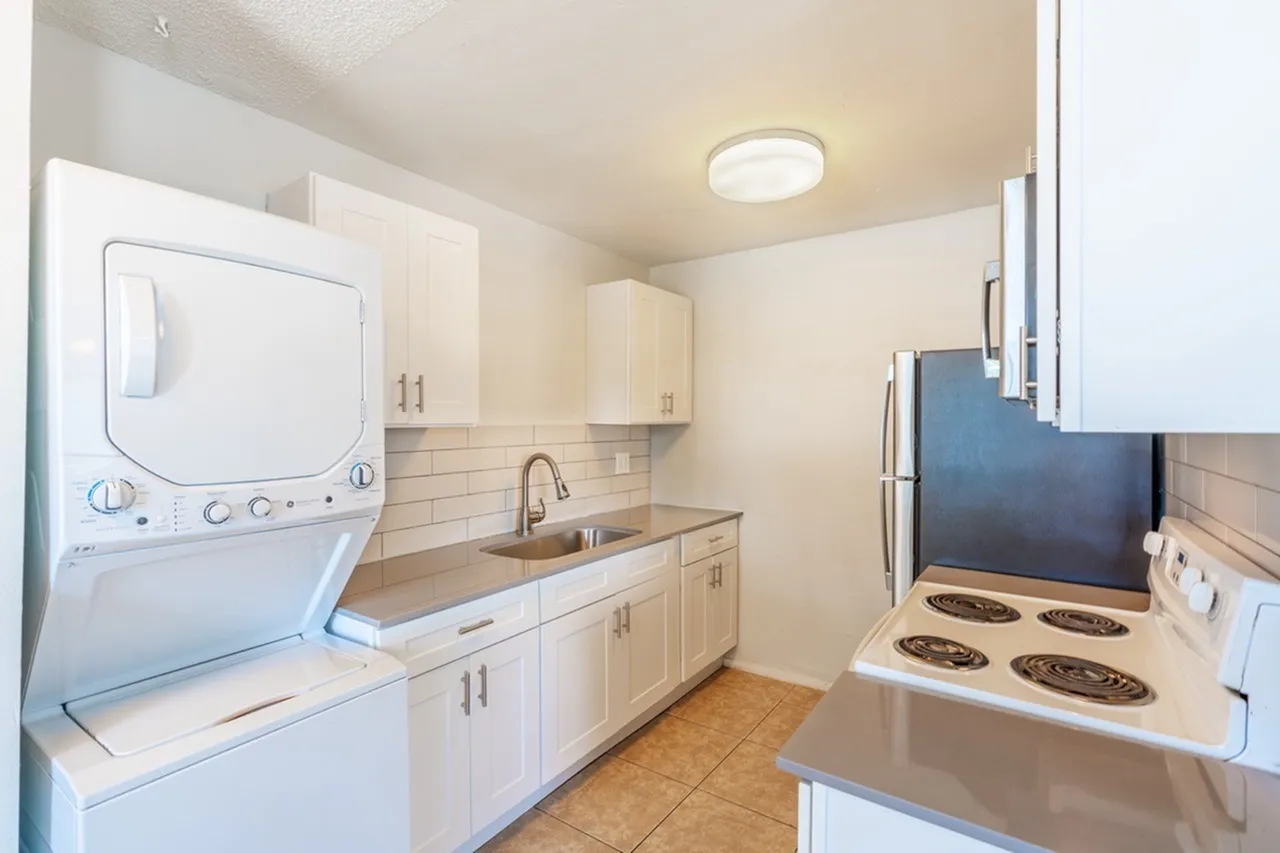 Kitchen with white cabinetry, stainless appliances, tile backsplash, wood-style plank flooring, stacked laundry appliances