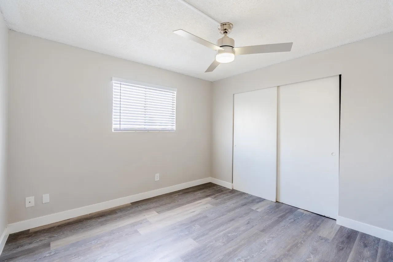 Primary bedroom, wood-style plank flooring, ceiling fan with light, sliding closet doors, window with blinds