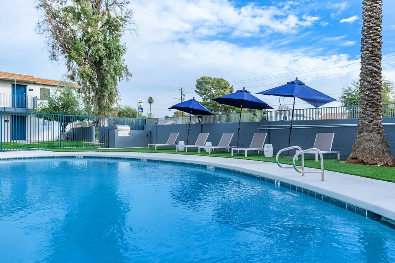 Resort pool with blue umbrellas, lounge chairs, palm tree, dark gray fence