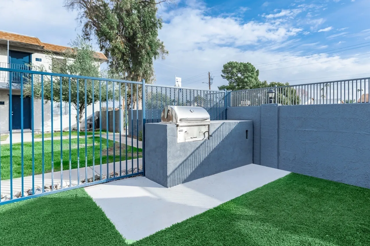 Concrete patio with grill, synthetic turf, blue metal railing and gate, gray composite fence