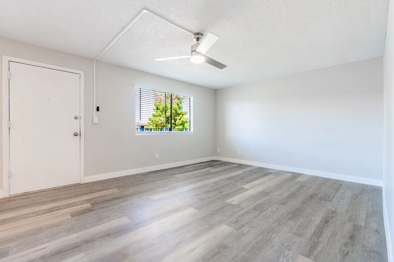Empty room with wood-style plank flooring, ceiling fan, entry door, window with blinds