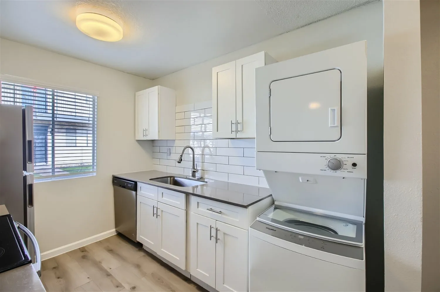 Laundry room with white cabinetry, subway tile backsplash, stainless appliances, wood-style plank flooring