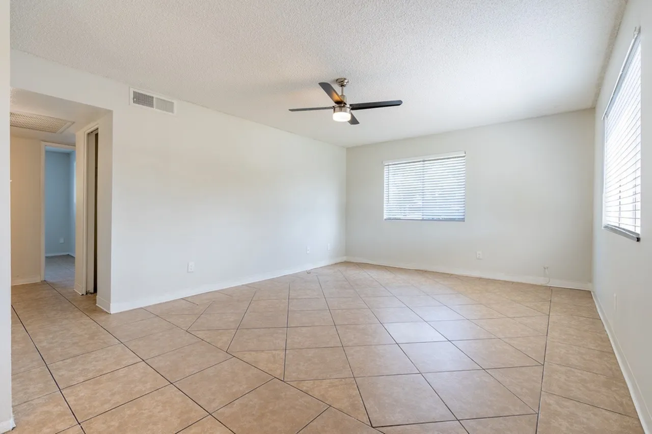Living room, wood-style plank flooring, ceiling fan, windows with blinds, entry door