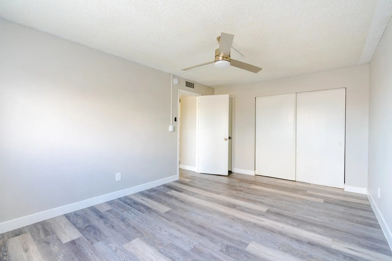Bedroom, wood-style plank flooring, ceiling fan, dual closet doors, white walls