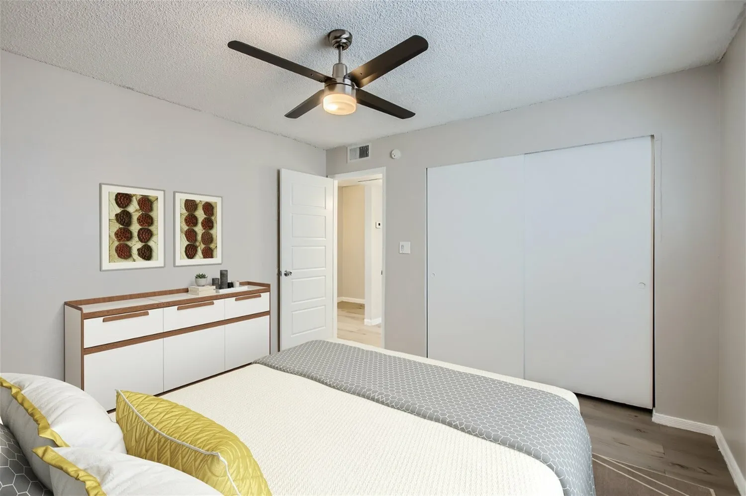 Primary bedroom, wood-style plank flooring, ceiling fan with light fixture, white dresser with wood trim