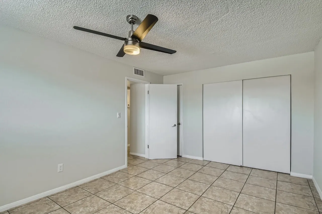 Bedroom, tile flooring, ceiling fan with light fixture, white closet doors, white walls