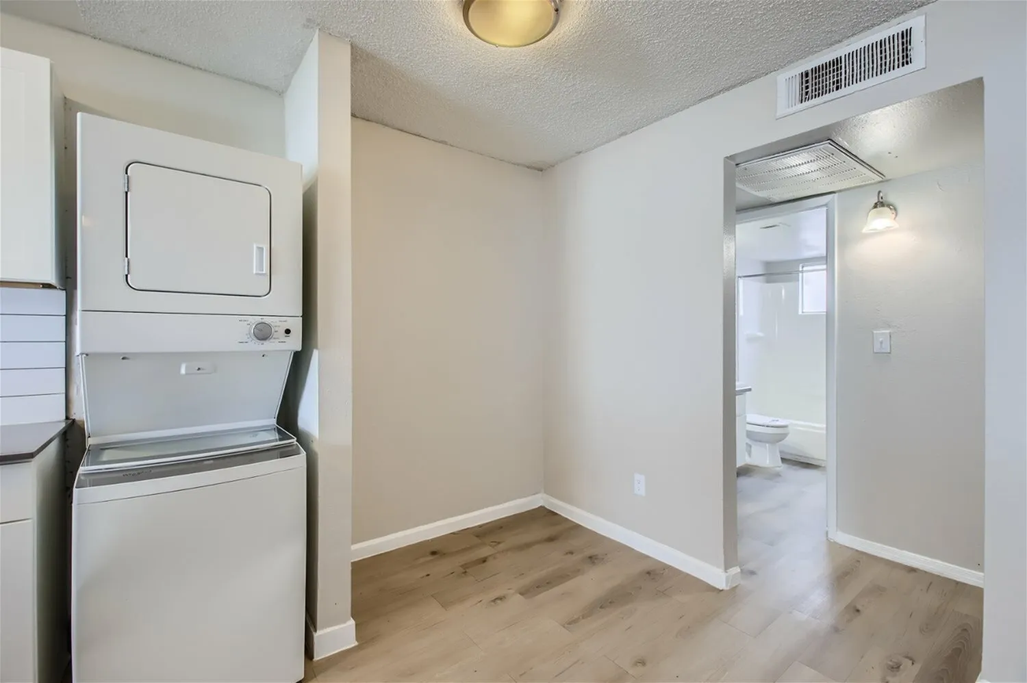 Laundry alcove with stacked washer dryer, wood-style plank flooring, bathroom access