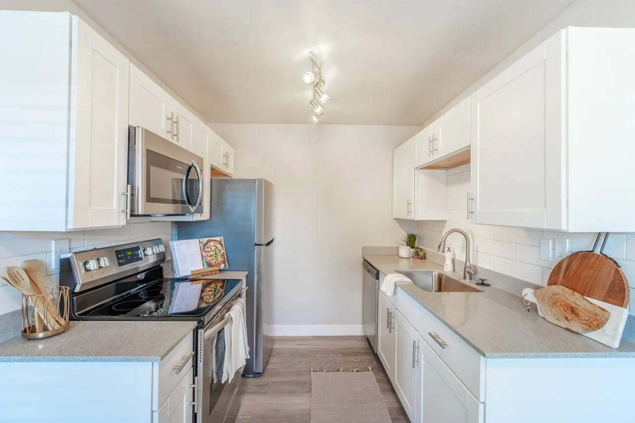 Galley kitchen, white shaker cabinetry, stainless appliances, gray countertops, wood-style plank flooring