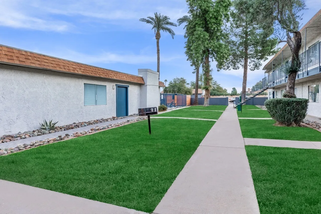 Courtyard with concrete sidewalk, green lawn, palm tree, white stucco building